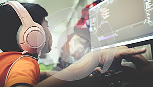 Asian kid coding and scripting program on on his game streaming desktop computer with headphone on