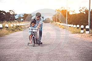 Asian kid girl having fun to ride bicycle with father