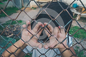 Asian kid girl low her head on a metal chain wire mesh fence.