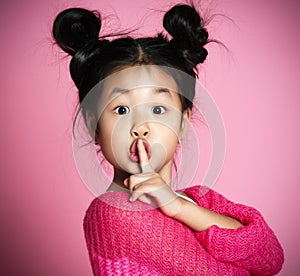 Asian kid girl in pink sweater shows shh sign Close up portrait