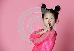 Asian kid girl in pink sweater shows shh sign Close up portrait