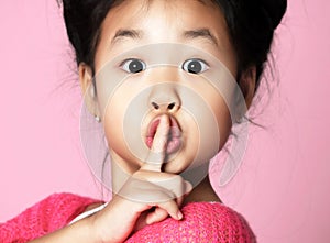 Asian kid girl in pink sweater shows shhh quiet sign on pink photo