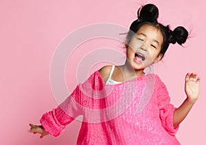 Asian kid girl in pink sweater, white pants and funny buns sings. close up.