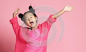 Asian kid girl in pink sweater, white pants and funny buns sings singing dancing on pink photo