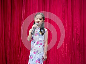 The Asian kid girl sing a song on stage at her school activity day, dress in Qipao style, red curtain background, contest of