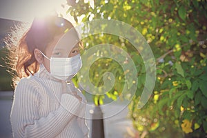 Asian kid girl wearing medical mask looking at the camera standing in the garden. To protect against coronavirus people wear a