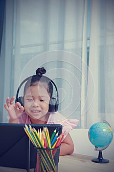 Asian kid girls wearing headphones learning distance by video calls online in the room from the home. Due to coronavirus pandemic