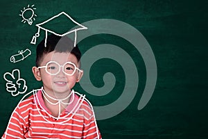 Asian kid imagine his graduated day with hand drawn graduate dress on green chalkboard background, education and graduation