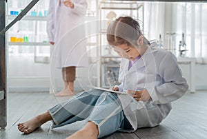 Asian kid playing digital tablet under table during learning with scientist in the laboratory. Disinterested and inattentive in