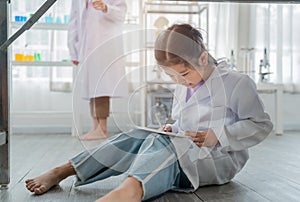 Asian kid playing digital tablet under table during learning with scientist in the laboratory. Disinterested and inattentive in photo
