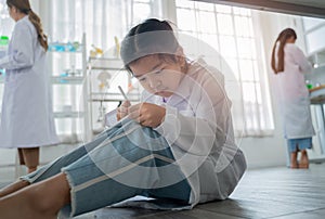 Asian kid playing digital tablet under table during learning with scientist in the laboratory. Disinterested and inattentive in photo