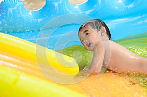 Asian kid playing in inflatable baby swimming pool on hot summer