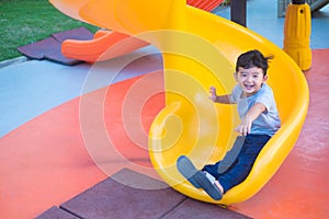 Asian kid playing slide at the playground under the sunlight in summer, Happy kid in kindergarten or preschool school yard
