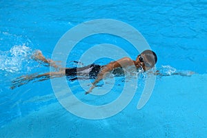 Asian kid swims in swimming pool - front crawl style with power scissor kick