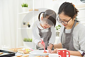 Asian Kid and young mother decorating cookies.