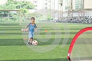 Asian  kindergarten boy, football player in soccer uniform is playing football at Training Session, Soccer Drills for Kids concept