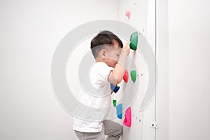 Asian kindergarten school boy having fun trying to climb on a small rock wall indoor at home, Physical, Hand and Eye Coordination