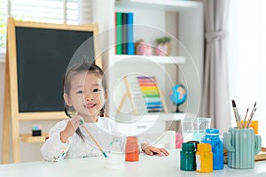 Asian kindergarten school girl looking at camera and smile while painting Plaster doll with Acrylic water color paint in living