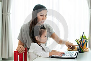 Asian kindergarten school girl  with mother video conference e-learning with teacher on laptop in living room at home.