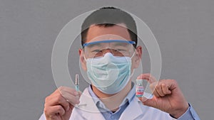 Asian Korean man doctor scientist in medical face mask show bottle of vaccine, show gesture thumbs up