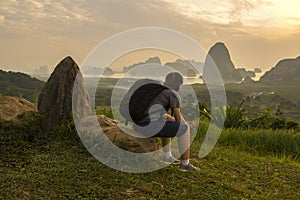 Asian lady with black bag sit on rock look at mountain and river view