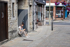 An Asian lady in her twenties looking at her mobile phone whilst sat on a step outside a shop