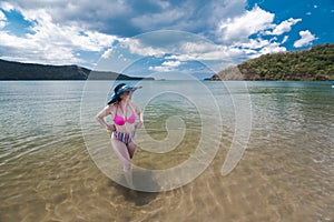 An asian lady in a high waist bikini admires the scenery at the beach. Adventure and weekend getaway theme