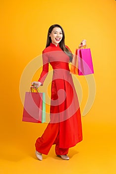 Asian lady in red ao dai dress holding shopping bags isolated on yellow background, Happy lunar new year