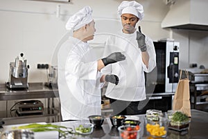 Asian and Latin chefs reading printed order while cooking meals in professional kitchen