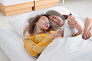 Asian lesbian lgbt couple lying on bed using tablet computer together in bedroom with happiness moment together,love wins concept