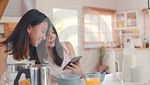 Asian Lesbian lgbtq women couple have breakfast at home, Young Asia lover girls happy using mobile phone check news while drink