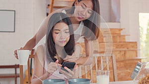 Asian Lesbian lgbtq women couple have breakfast at home, Young Asia lover girls happy using mobile phone check news while drink