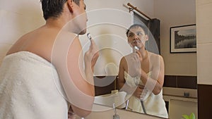 Asian LGBT  ladyboy  in towel shaving in bathroom. gay man looking into mirror when doing routine grooming.