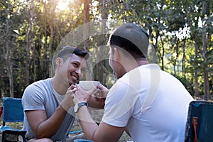 Asian LGBTQ couple drinking coffee in a romantic camping tent. LGBTQ couple drinking coffee in a camping tent, enjoying