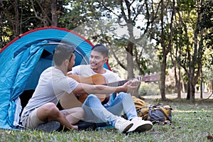 Asian LGBTQ couple enjoying nature, camping with tents in the forest area by the river, playing guitar.