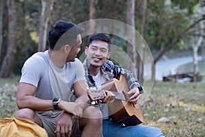 Asian LGBTQ couple enjoying nature, camping with tents in the forest area by the river, playing guitar.