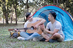 Asian LGBTQ couple enjoying nature, camping with tents in the forest area by the river, playing guitar.