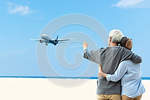 Asian Lifestyle senior couple hug and pointing the landing planes or airplane on the beach