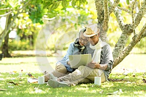 Asian Lifestyle senior elderly retire couple drinking coffee and work from home online in the nature park happy and relax time.