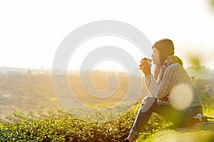 Asian lifestyle women wearing sweater, sitting and drinking hot coffee or tea relax outdoor in the sunrise morning sunny day at te