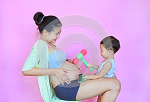 Asian little baby boy playing with baby in tummy of pregnant mother isolated on pink background. Kid play hit belly by plastic