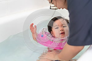 Asian little baby girl swimming and wear rubber ring on neck in bathtub, Mother holding daughter for safety support, Living