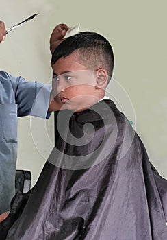 Asian little boy being shaved by barber at the barbershop