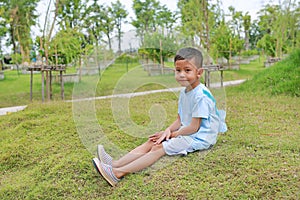 Asian little boy child looking camera and sitting on green grass in the garden