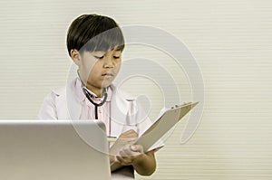 Asian Little boy Doctor holding board, To analyze patient data, laptop placed on table. With copy space