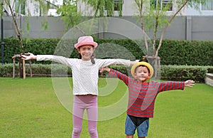 Asian little boy and girl child wearing straw hat standing and open wide arms with looking camera in the garden