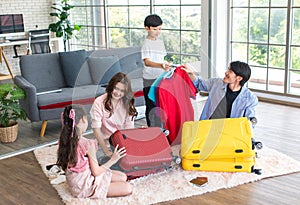 Asian little boy and girl helping father and mother preparing packing clothes and stuff into trolley luggages on living room