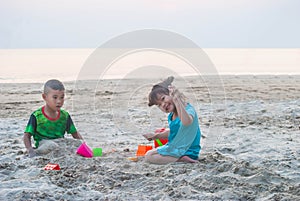 Asian little boy and girl are playing together on the sandy beach.