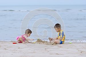 Asian little boy and his baby sister playing together on the sandy beach.