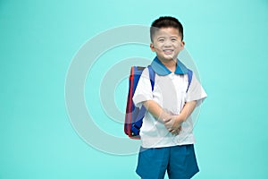 Asian little boy in a school uniform with backpack having fun isolated on green background.